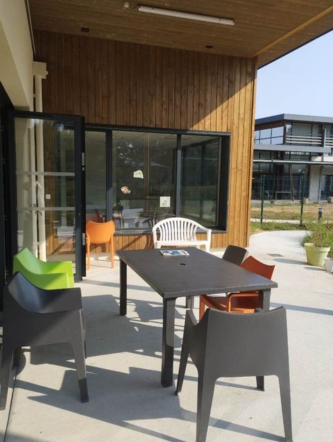 Terrasse extérieure avec table et chaises noires à côté d'un bâtiment en bois et de portes vitrées sous un soleil éclatant