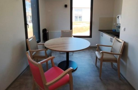 Petite salle de réunion avec une table ronde et trois chaises en bois, dont une avec un coussin rose.