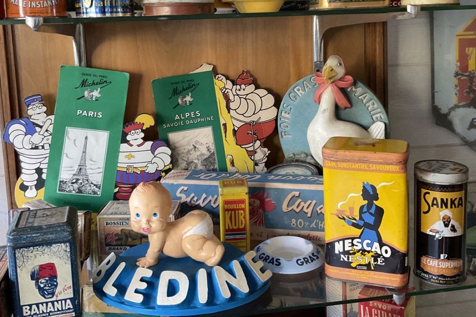 Étagère remplie d'objets publicitaires vintage, comprenant une statuette de bébé, des boîtes en fer-blanc et des panneaux.