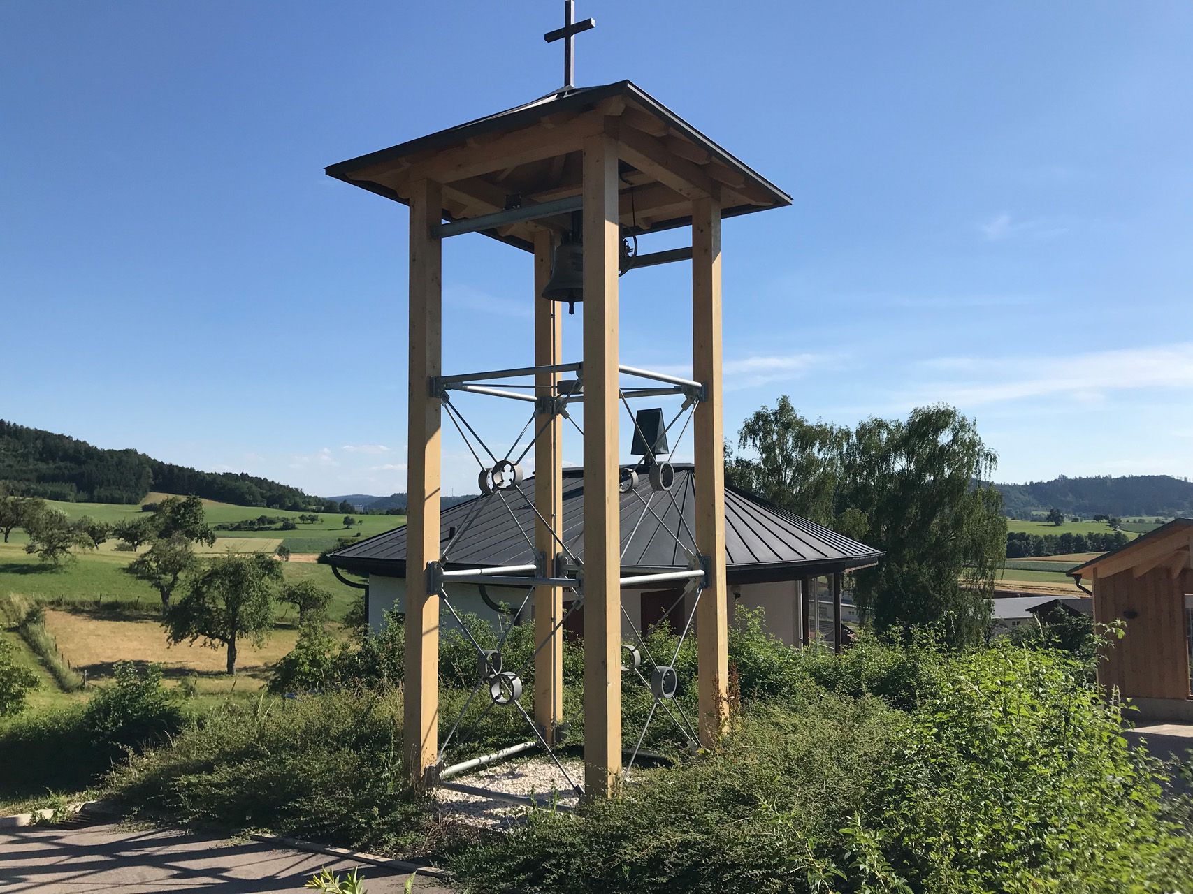 Ein hölzerner Glockenturm mit einem Kreuz darauf.