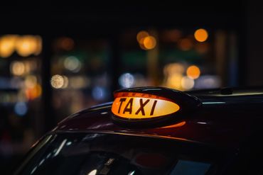 Panneau TAXI jaune lumineux sur le toit d'une voiture, la nuit, avec les lumières de la ville floues en arrière-plan.