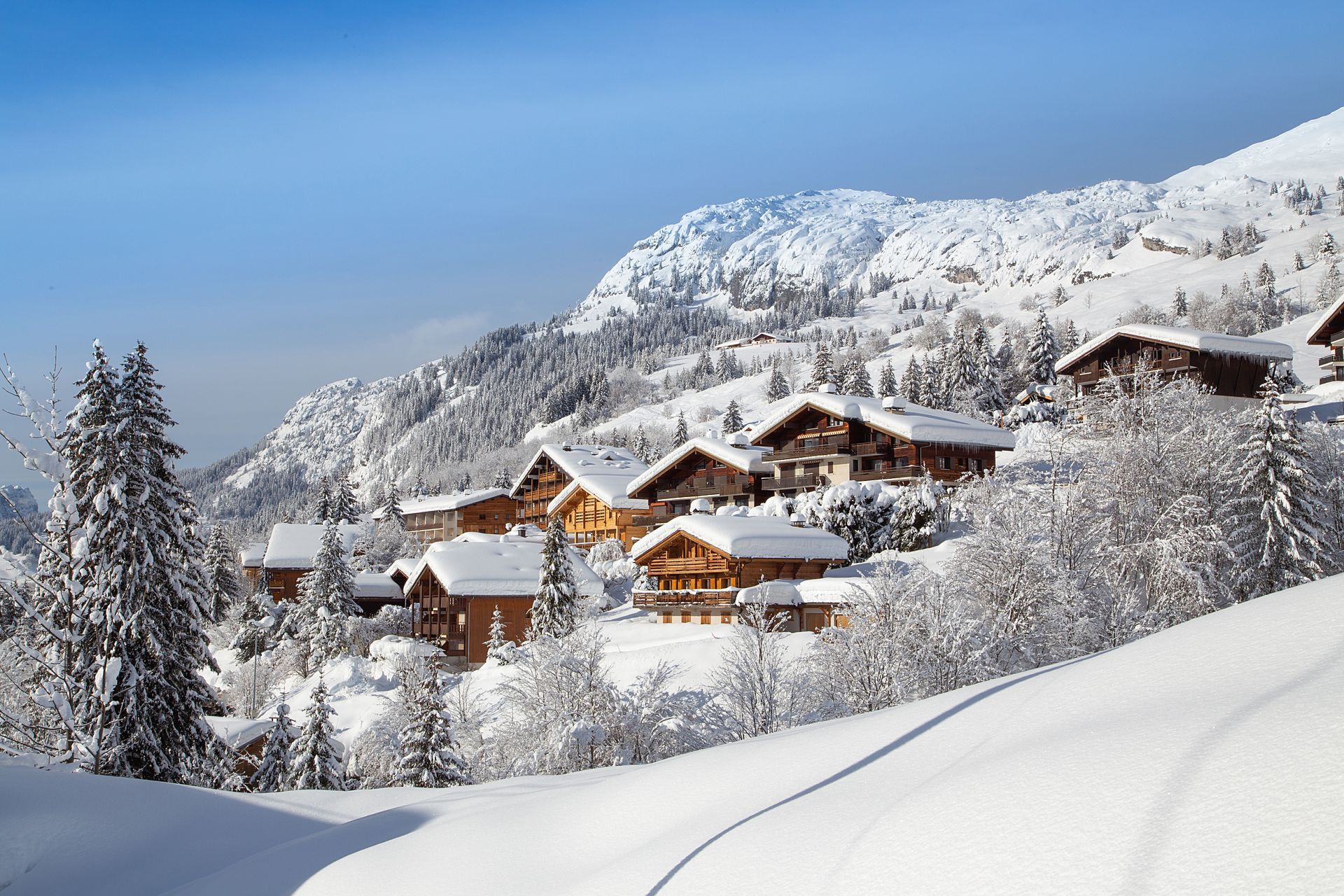 Village alpin enneigé avec ses chalets en bois et ses montagnes sous un ciel d'un bleu limpide.