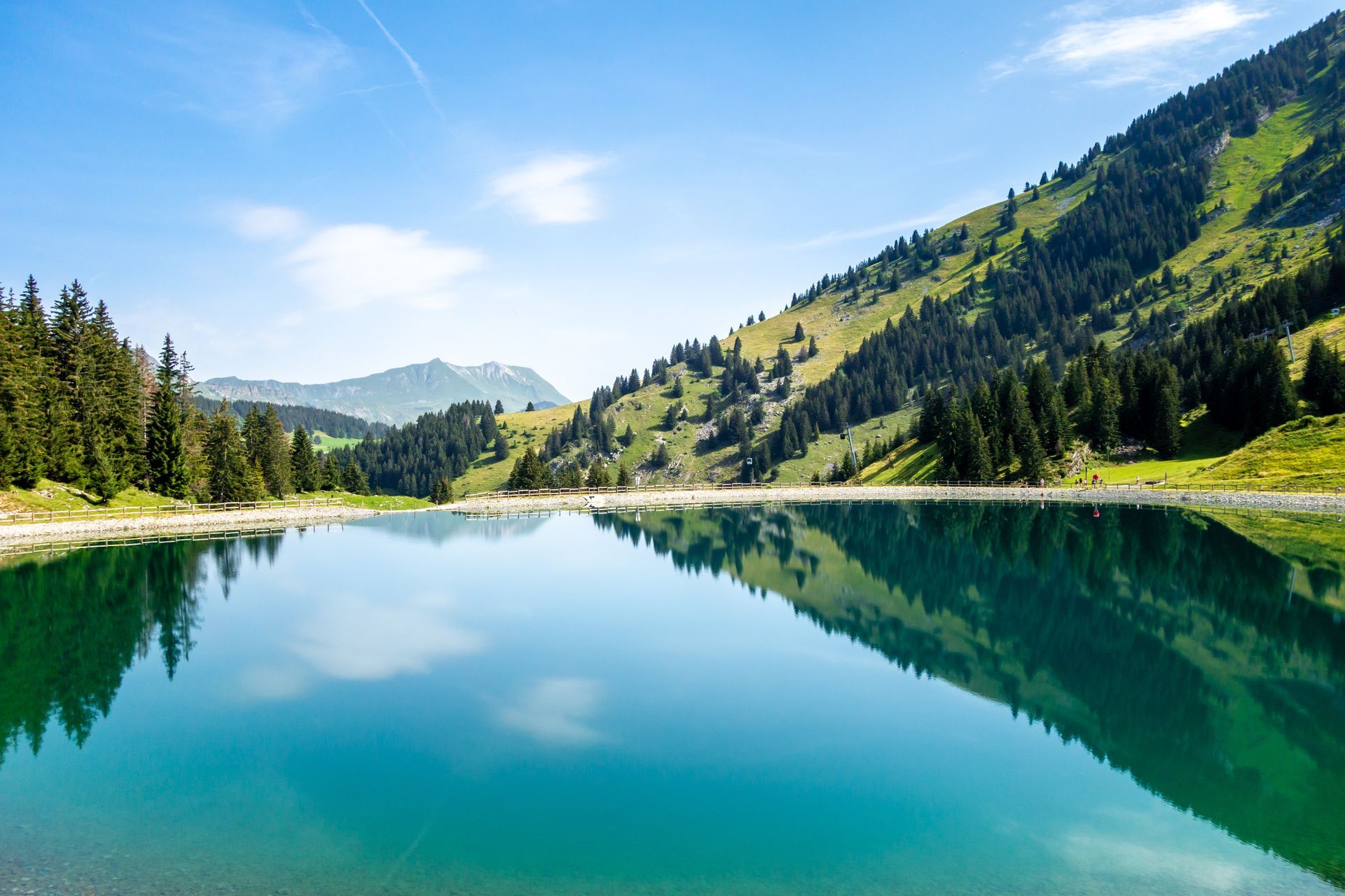 Lac de montagne limpide reflétant les pentes boisées et le ciel bleu par une journée ensoleillée.