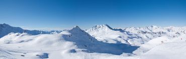 Chaîne de montagnes enneigées sous un ciel d'un bleu limpide, avec des sommets ensoleillés et d'épais champs de neige blanche.