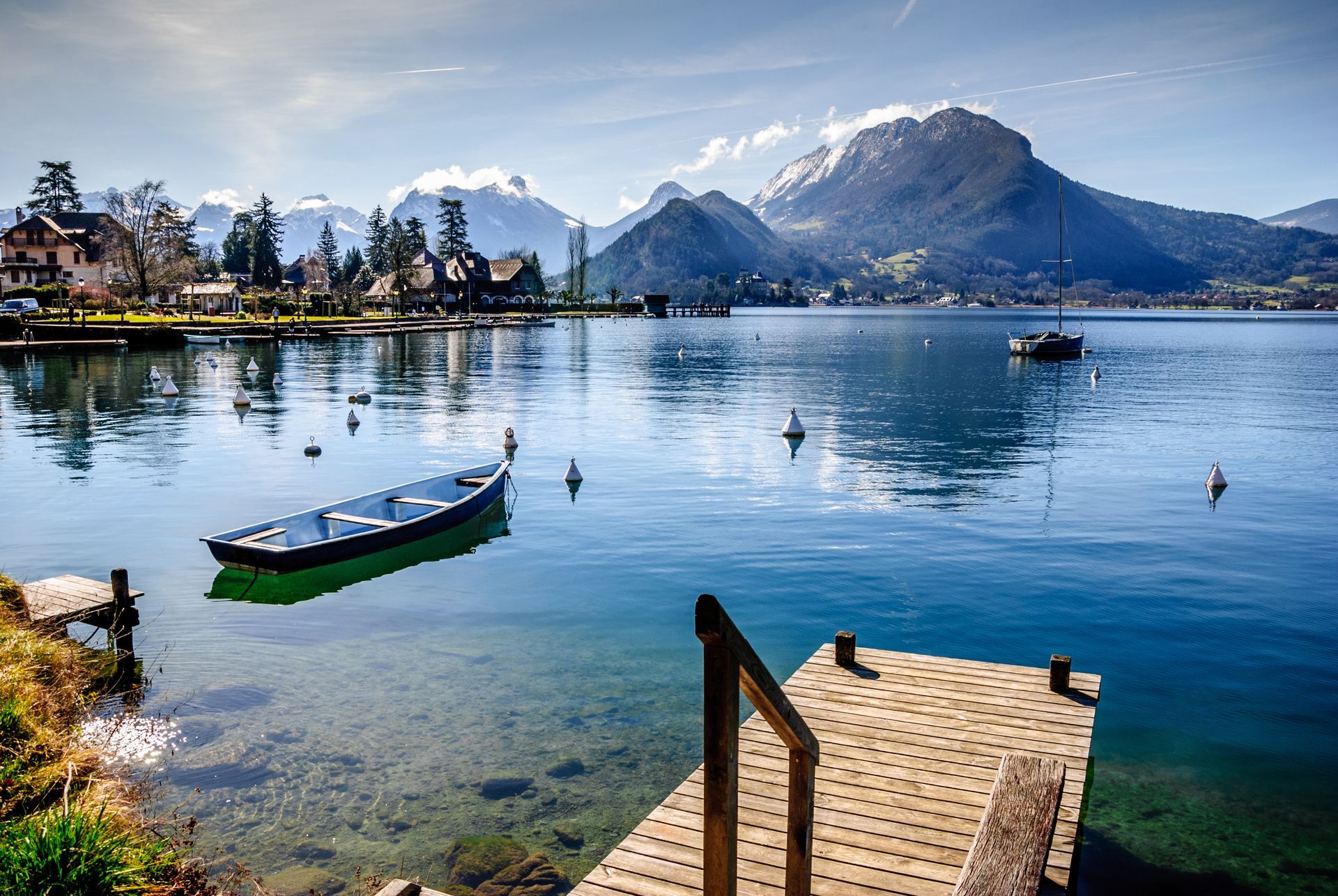 Lac avec une petite barque, un quai en bois et des reflets de montagnes sous un ciel bleu clair.