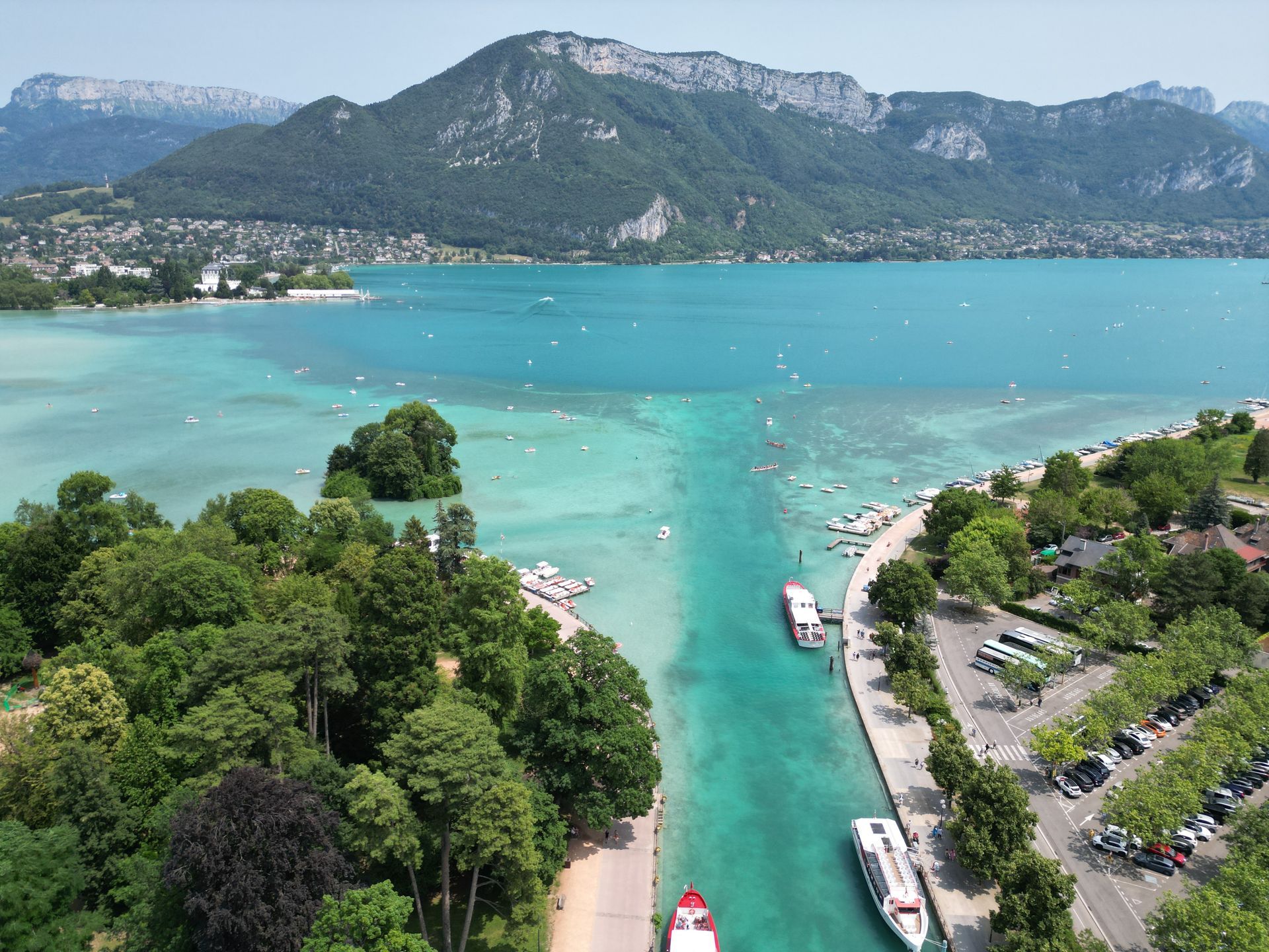 Une anse lacustre turquoise avec des bateaux, bordée de montagnes verdoyantes sous un ciel dégagé.