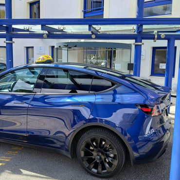 Une berline Tesla bleue est garée sous un auvent à l'extérieur d'un bâtiment.