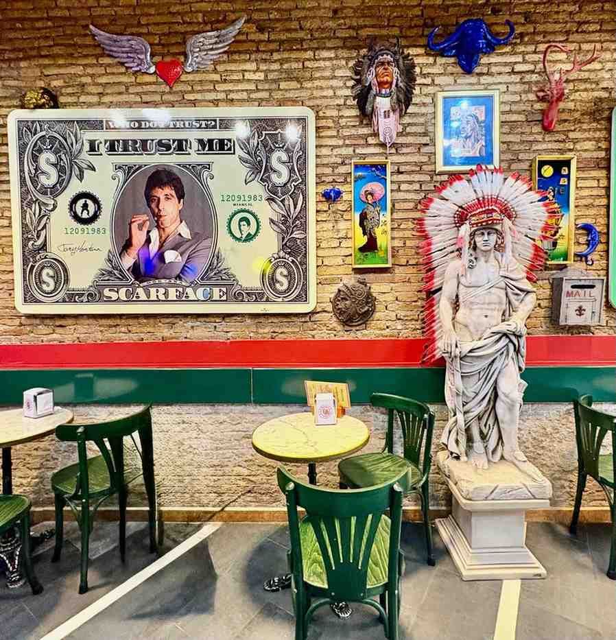 Exhibición de pared con varias obras de arte enmarcadas sobre fondo azul. Incluye un retrato naranja con detalles dorados.