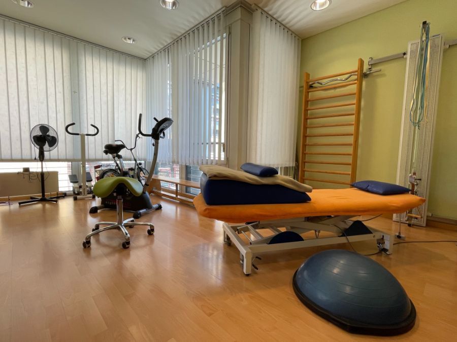 Physiotherapieraum mit Trainingsgeräten: Laufband, Heimtrainer, Massagetisch, Sprossenwand und Balanceball.
