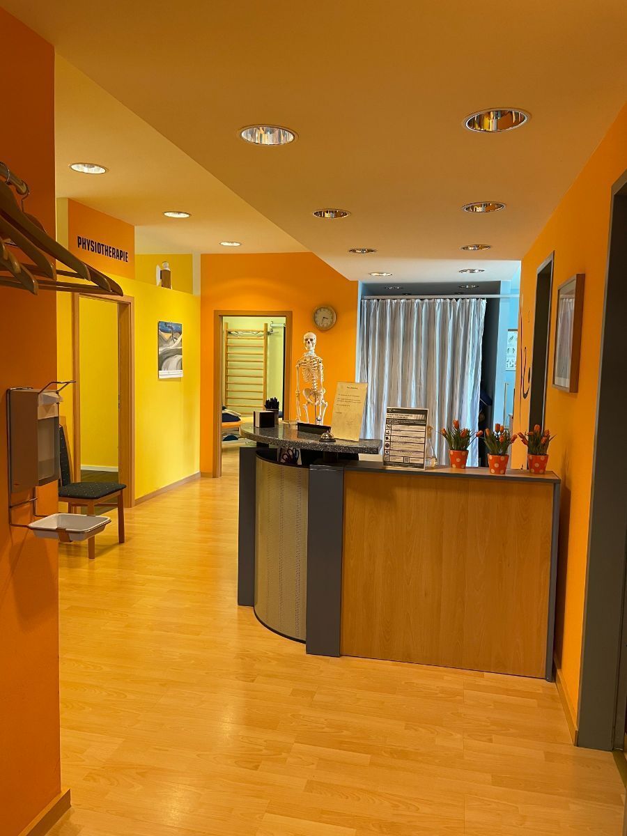 Hell erleuchteter orangefarbener Empfangsbereich mit Holzböden, Schreibtisch und einem Flur, der zu anderen Räumen führt.