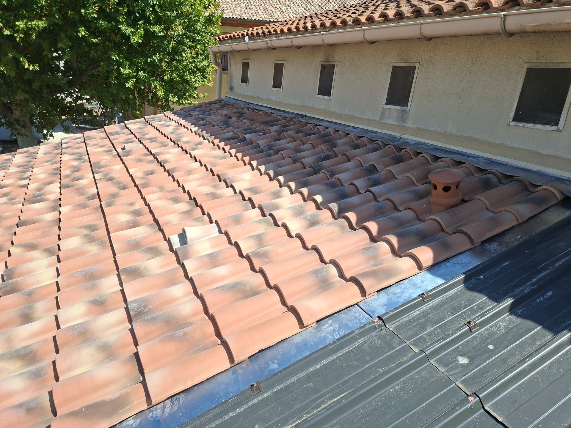Maison beige de deux étages avec toit de tuiles rouges, soubassement en pierre et allée gravillonnée. 