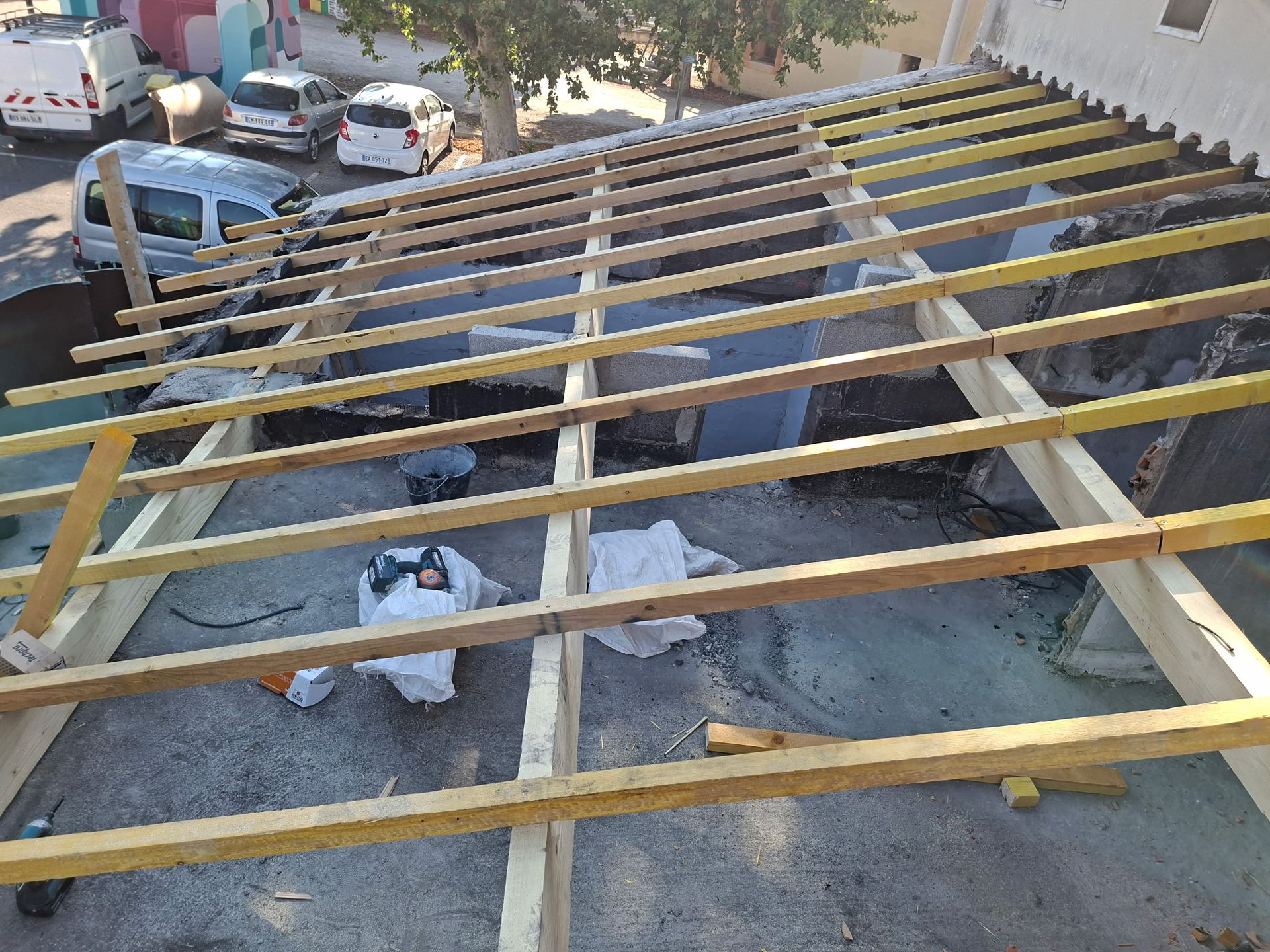 Maison en construction, ouvriers sur le toit, échafaudage, tas de briques, bétonnière, poubelle jaune.