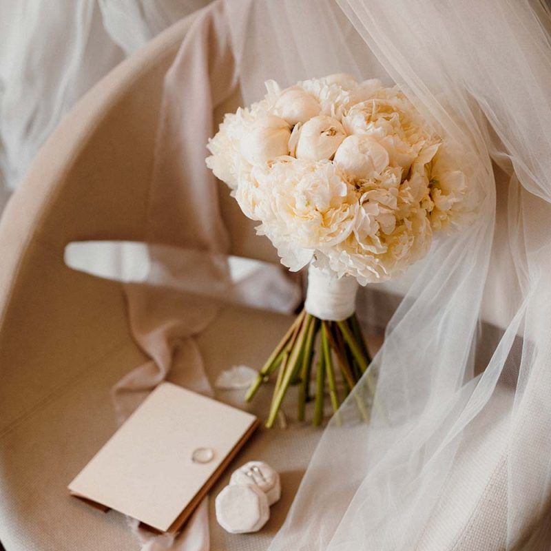 Un bouquet de fleurs blanches est posé sur une chaise à côté d'un voile et d'anneaux.