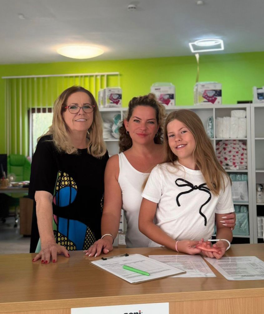 Drei Personen stehen hinter einem Tresen in einem Laden mit Regalen voller Produkte.