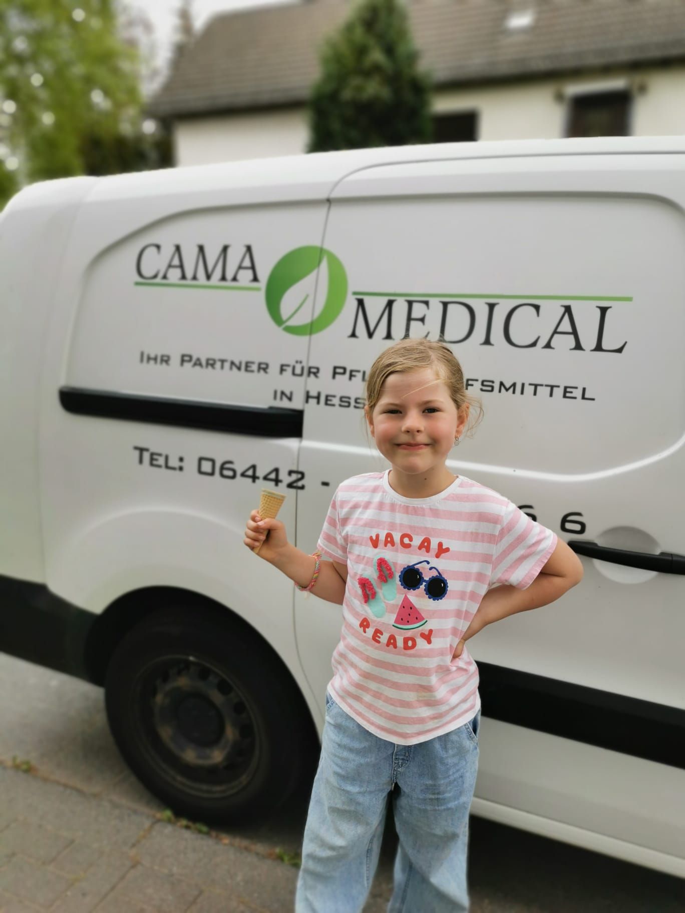 Mädchen mit Eiscreme steht lächelnd neben einem weißen Lieferwagen mit dem Logo „CAMA MEDICAL“.
