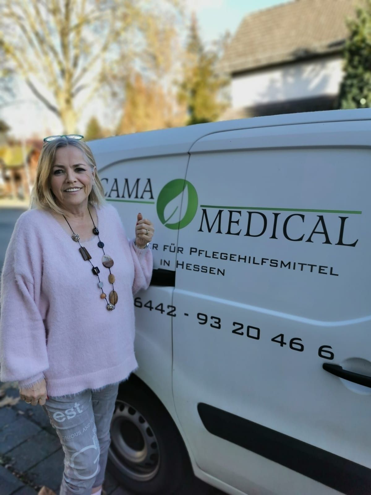 Eine Frau neben einem Lieferwagen mit dem Logo „Cama Medical“ zeigt den Daumen nach oben.