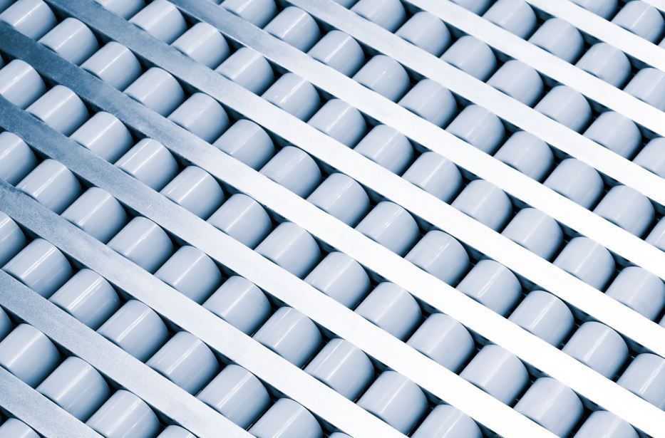 Cinta transportadora con filas diagonales de rodillos blancos y vigas de soporte plateadas.