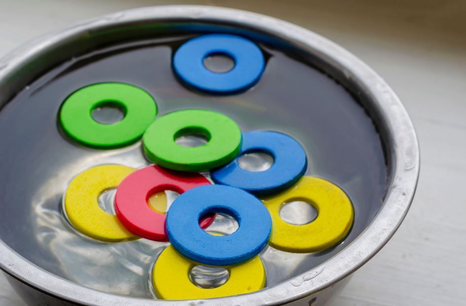 Anillos flotantes de colores en un recipiente de metal lleno de agua.