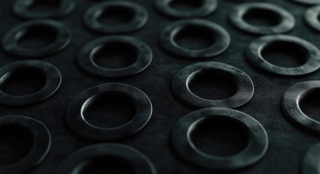 Arandelas de metal negro dispuestas en forma de cuadrícula sobre una superficie oscura.