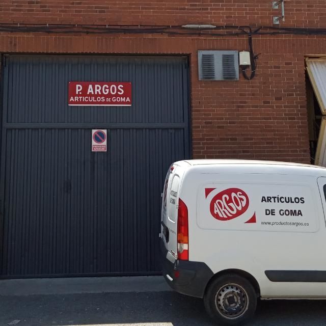 Una camioneta de reparto estacionada frente a la puerta de un almacén gris con el nombre de la empresa