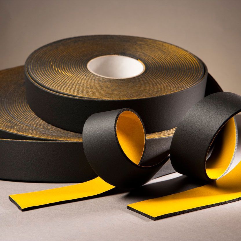 Rollos de cinta de espuma de color negro con respaldo amarillo, sobre una superficie gris.