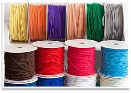 Varios carretes de cordón de colores, incluidos amarillo, naranja, morado, beige, verde, gris, marrón, rojo, azul y blanco.