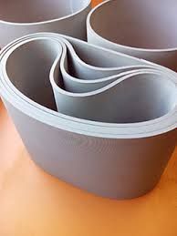 Cintas transportadoras de caucho gris apiladas en un patrón curvo abstracto.