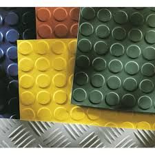 Muestras variadas de pisos de caucho en varios colores, incluidos verde, amarillo, marrón y azul, sobre una lámina de metal texturizada.