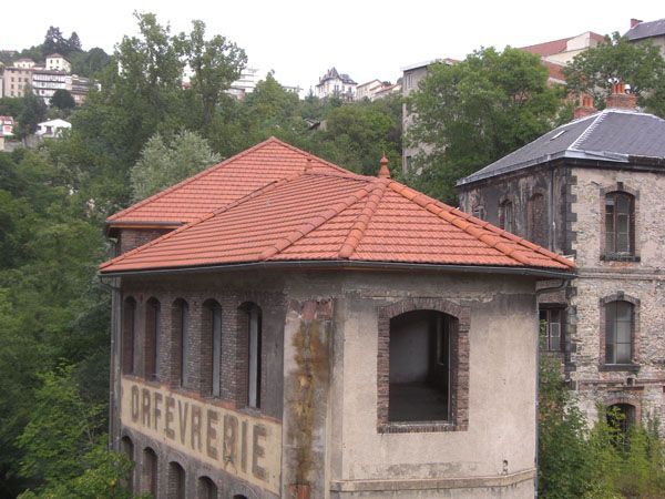 Vieille bâtisse en pierre aux fenêtres cintrées et au toit de tuiles rouges, dans un village niché sur une colline verdoyante