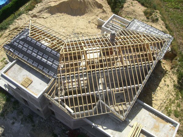 Vue aérienne d’une maison en construction, avec sa charpente en bois apparente et ses murs en béton.