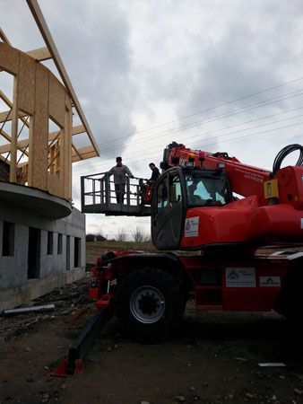Un chariot télescopique rouge élève des ouvriers sur une nacelle suspendue à côté d’un bâtiment en construction