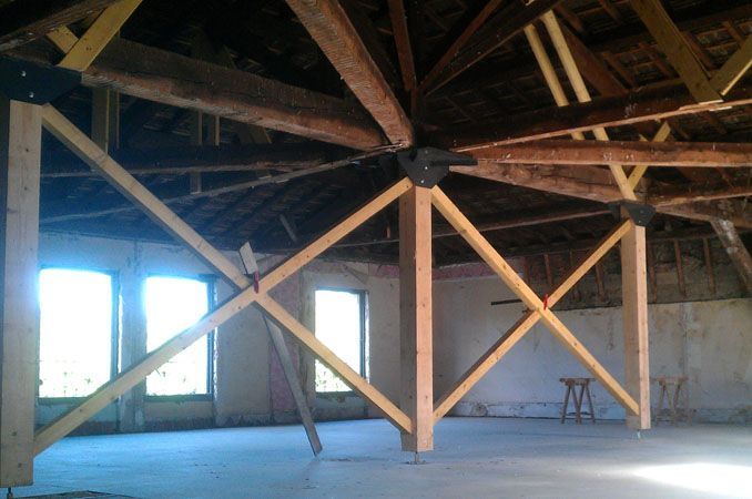 Combles vides avec une charpente apparente en bois et des fenêtres à cadre bleu, éclairés par la lumière du jour