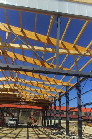 Chantier avec une ossature en acier et des poutres de toit jaunes sous un ciel bleu éclatant