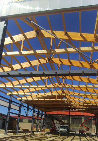 Charpente métallique en cours de construction, avec des poutres en bois et un ciel bleu visible à travers le toit ouvert.