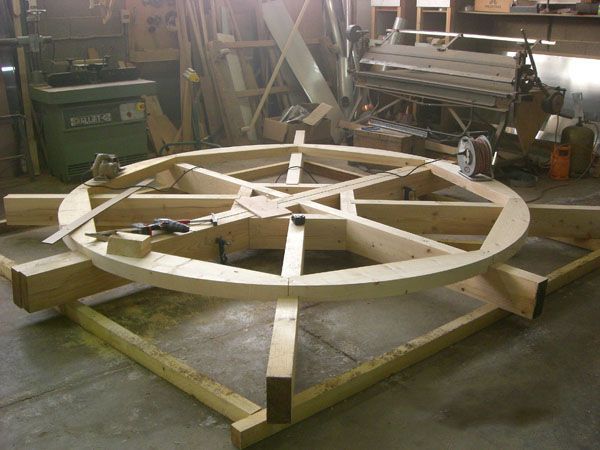 Grande structure de roue en bois en cours de fabrication dans un atelier, posée sur un support.