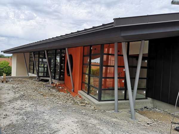 Extérieur d’une maison moderne en construction, avec un toit en pente, de grandes baies vitrées et des touches d’orange