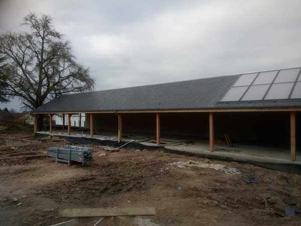 Long bâtiment bas doté de panneaux solaires sur le toit, sur un chantier boueux et couvert de nuages
