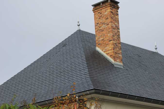 Cheminée en briques sur un toit gris recouvert de bardeaux, sous un ciel nuageux