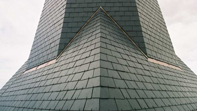 Angle d’un bâtiment revêtu de bardeaux gris, avec des toits pentus et un sommet central pointu
