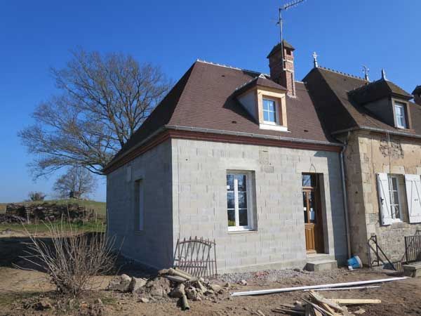 Façade d’une maison en pierre avec un toit en pente, des fenêtres et une porte en bois, par une journée ensoleillée.