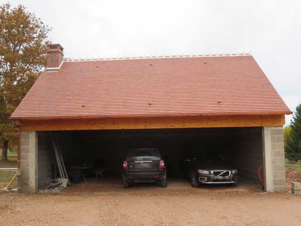 Garage ouvert avec deux voitures garées sous un toit de tuiles rouges
