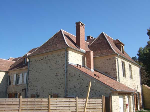Maison en pierre au toit de tuiles rouges et à la haute cheminée, sous un ciel bleu dégagé