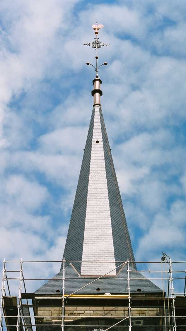 Grand clocher d’église argenté surmonté d’une girouette sur fond de ciel bleu nuageux