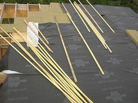 Toiture en cours de construction, avec une sous-couche noire et des panneaux isolants jaunes, sur lesquels sont posés des liteaux en bois