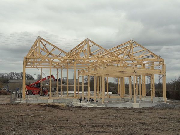 Ossature d’une maison en bois en cours de construction sur des fondations en béton, sous un ciel nuageux