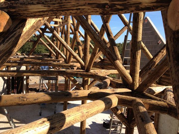 Des poutres en bois et des supports en corde composent une structure rustique en bois sur fond de ciel bleu.