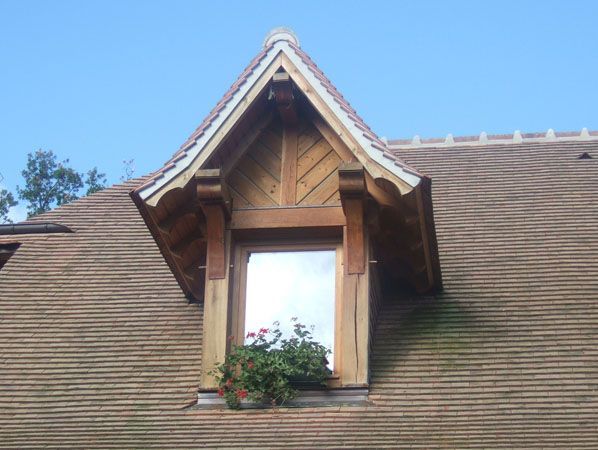 Fenêtre en lucarne avec encadrement en bois et jardinière sur un toit en bardeaux, sur fond de ciel bleu