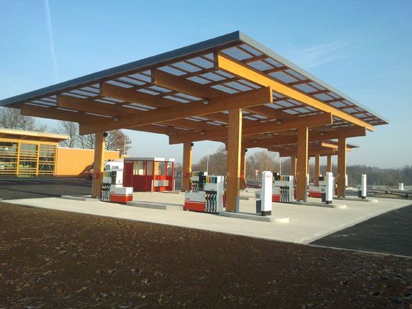 Auvent moderne de station-service avec des pompes à carburant et des équipements rouges et blancs sur un parking goudronné, sous un ciel dégagé