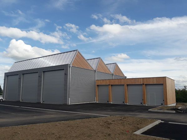 Rangée d’abris de stockage métalliques modernes aux portes grises, sous un ciel bleu nuageux