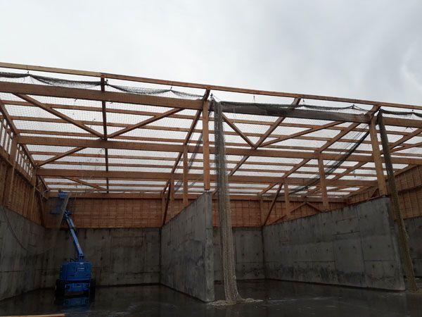 Hangar en béton ouvert sur les côtés, avec une charpente de toit en bois et un pont élévateur bleu à l’intérieur